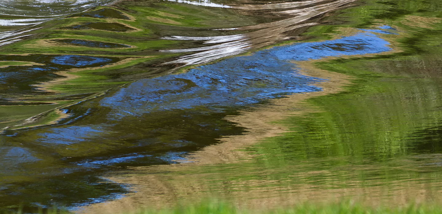 A tidal bore on the River Dee with reflections of the banks and sky.
